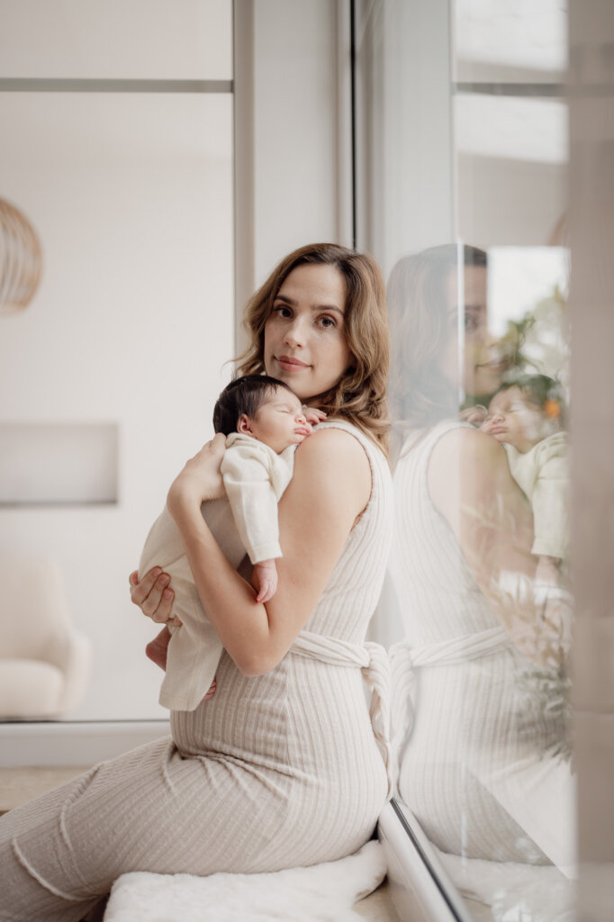 Babyfotos Mama sitzt mit Baby auf der Fensterbank und sie kuscheln