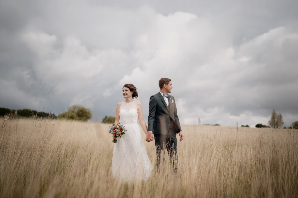 Paar steht auf einem Feld hält die Hände und guckt sich nicht an.