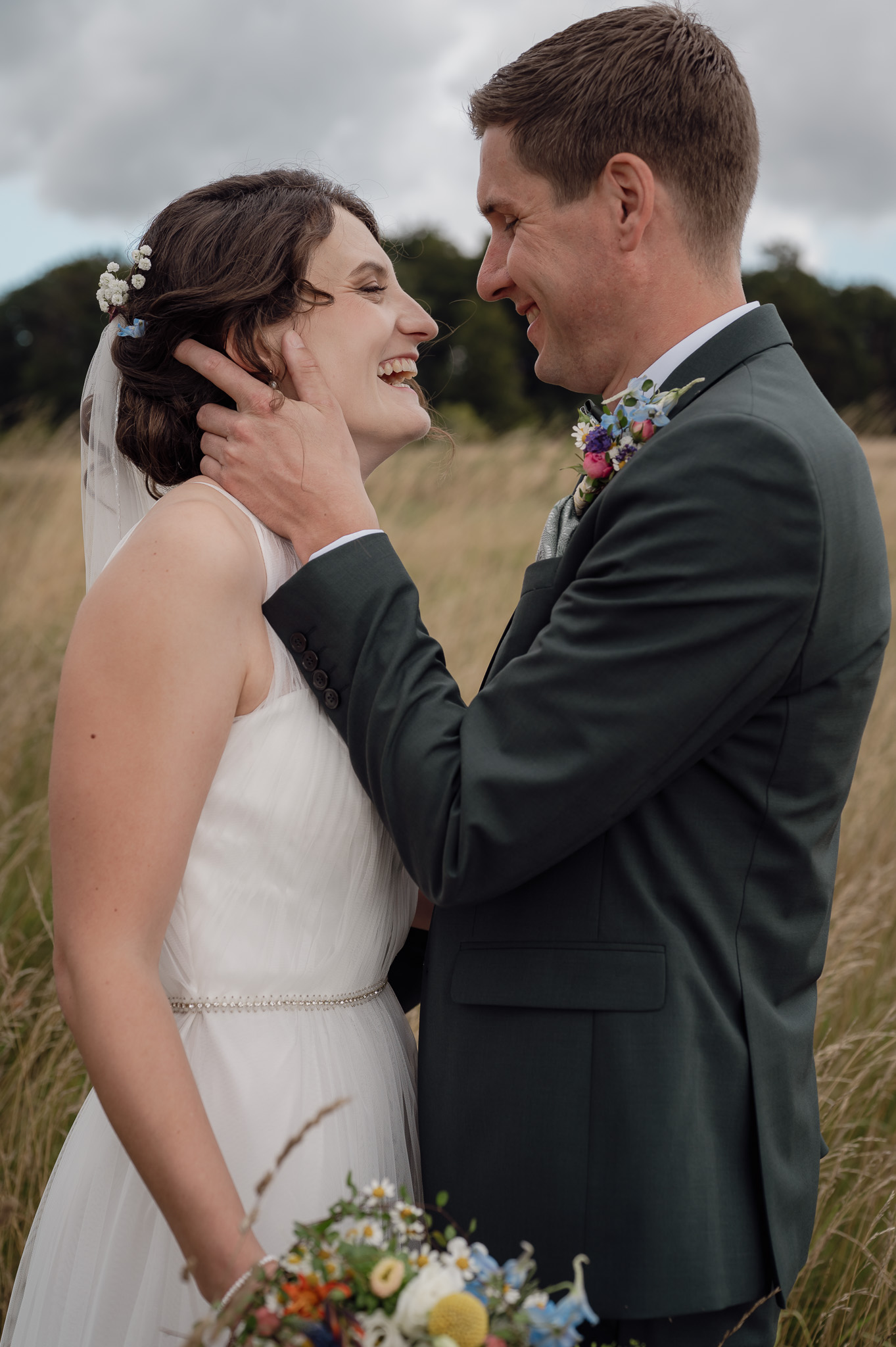 Brautpaar steht sich gegenüber und er legt die Hand in ihren Nacken und sie lacht