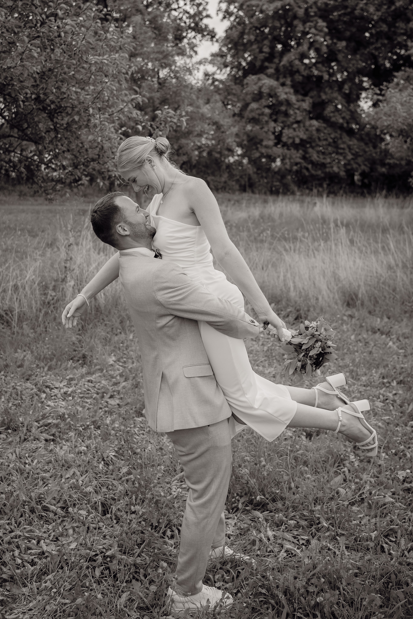 Der Bräutigam hebt seine Braut hoch und sie genießt es ganz lässig, hält sich nicht fest, während der Hochzeitsfotograf Göttingen das Paar im Gras fotografiert