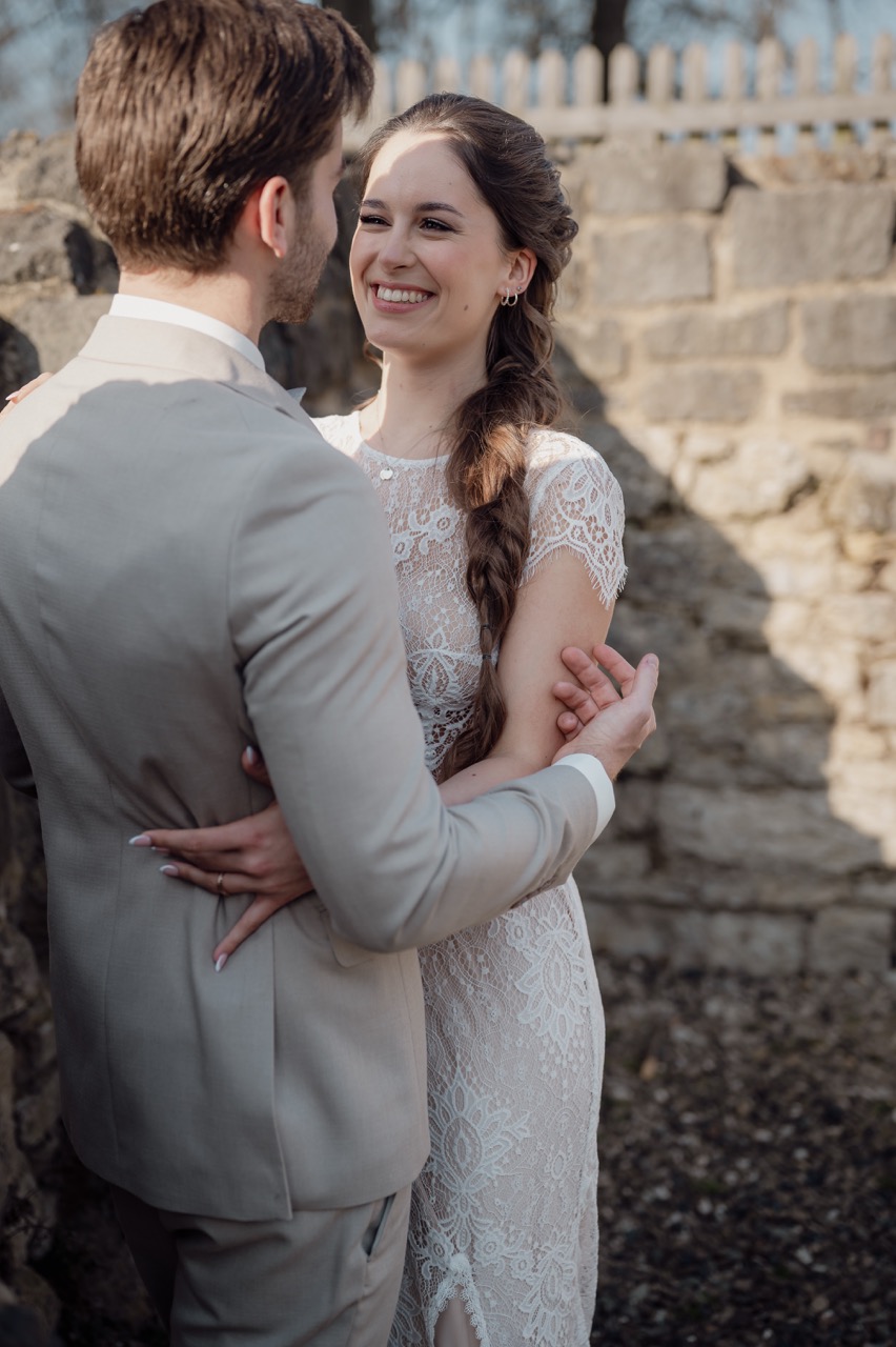 Brautpaar steht sich gegenüber in der Burgruine und lächelt sich an, während er ihren Arm streichelt