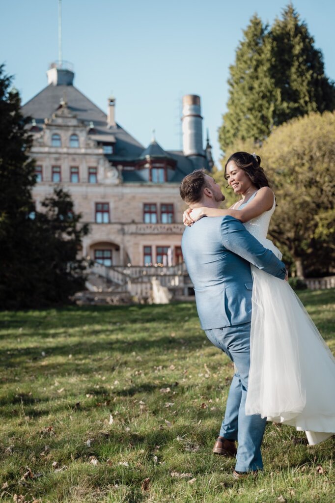 Hochzeitsfoto von Mann nimmt Frau auf den Arm vor dem Schloss Wolfsbrunnen