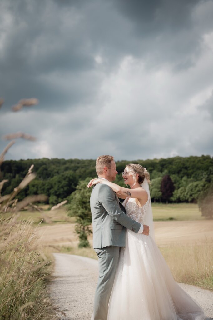 Brautpaar steht auf dem Feldweg und sie legt ihre Arme um ihn