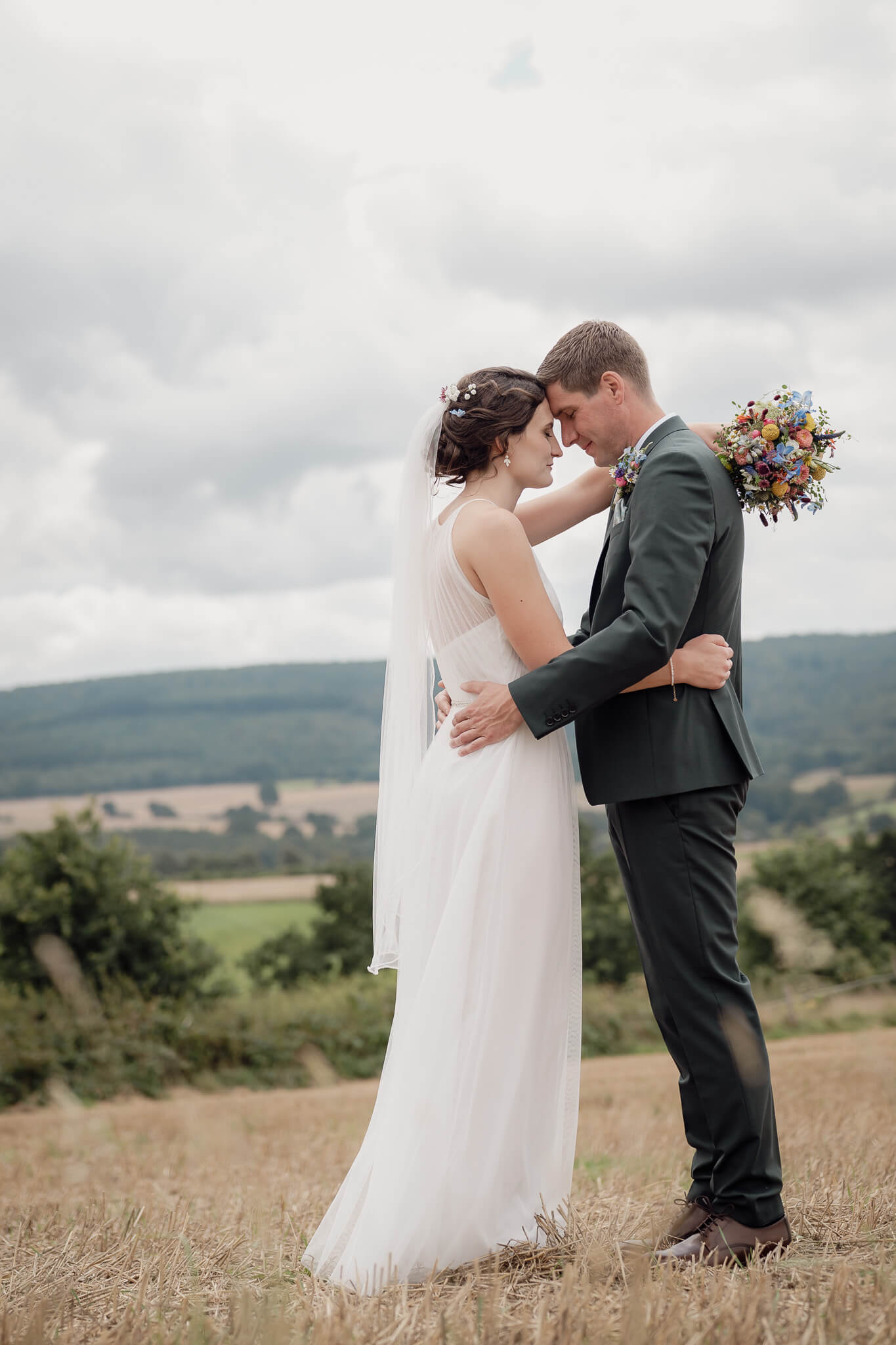 Hochzeitsfoto des Brautpaar welches auf dem Feld mit Stoppeln steht und schaut sich tief in die Augen und ist Stirn an Stirn 