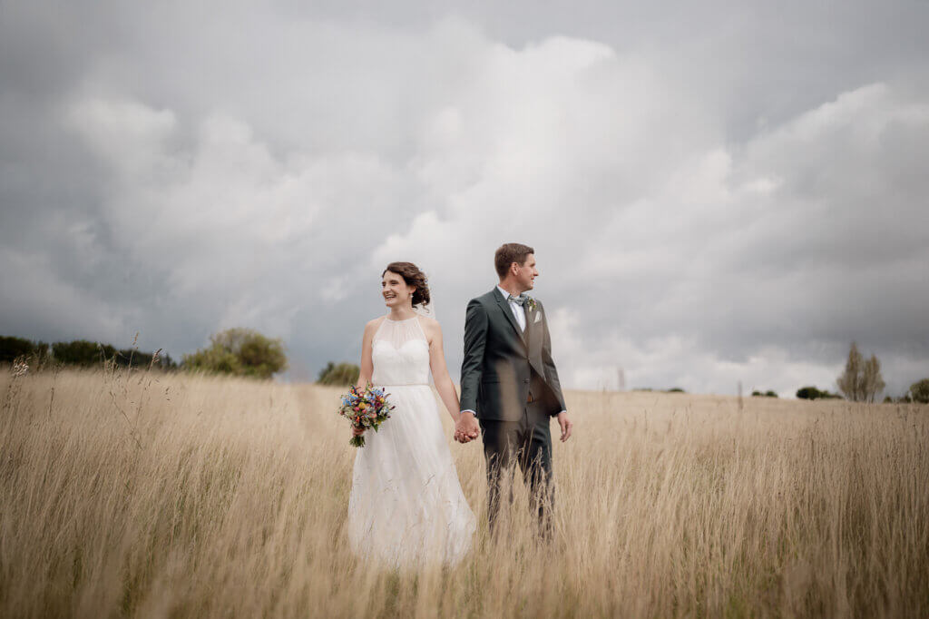 Paar steht auf einem Feld hält die Hände und guckt sich nicht an.