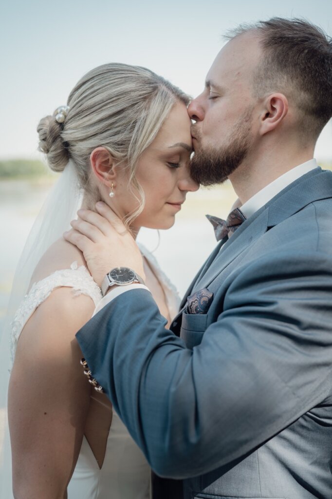 Bräutigam küsst die Braut liebevoll auf die Stirn und streichelt sie dabei im Nacken