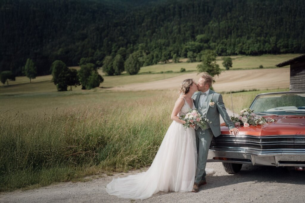 Brautpaar steht auf einem Feldweg mit Auto und küsst sich