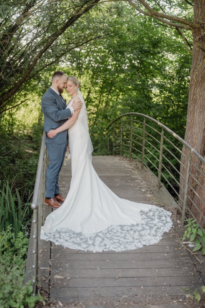 Brautpaar steht auf der Brücke und kuschelt im Sommer unter einem Baum