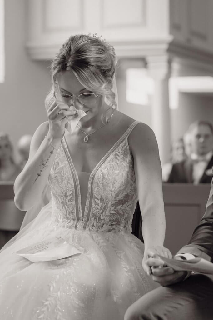 Hochzeitsvideo Österreich fotografiert die in der Kirche sitzende und weinende Braut, während sie sich eine Träne weg wischt